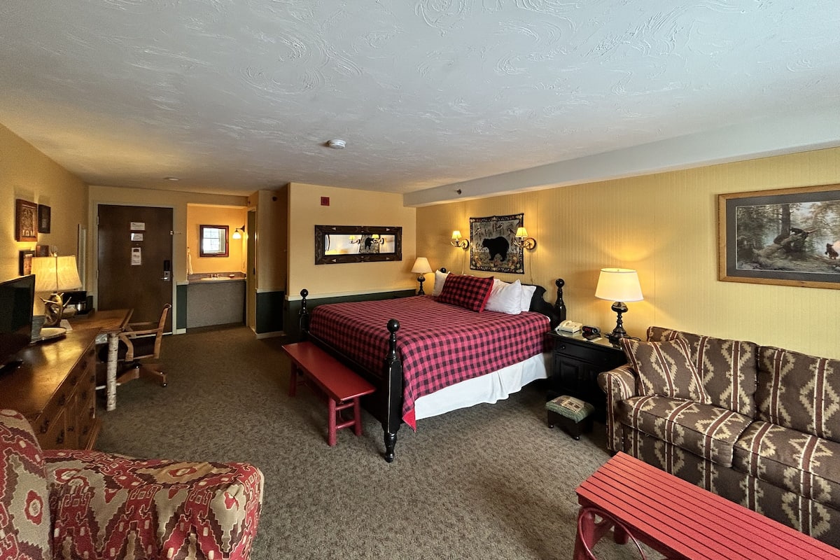 A hotel room with a bed, a desk, a chair, a sofa, and a bench.