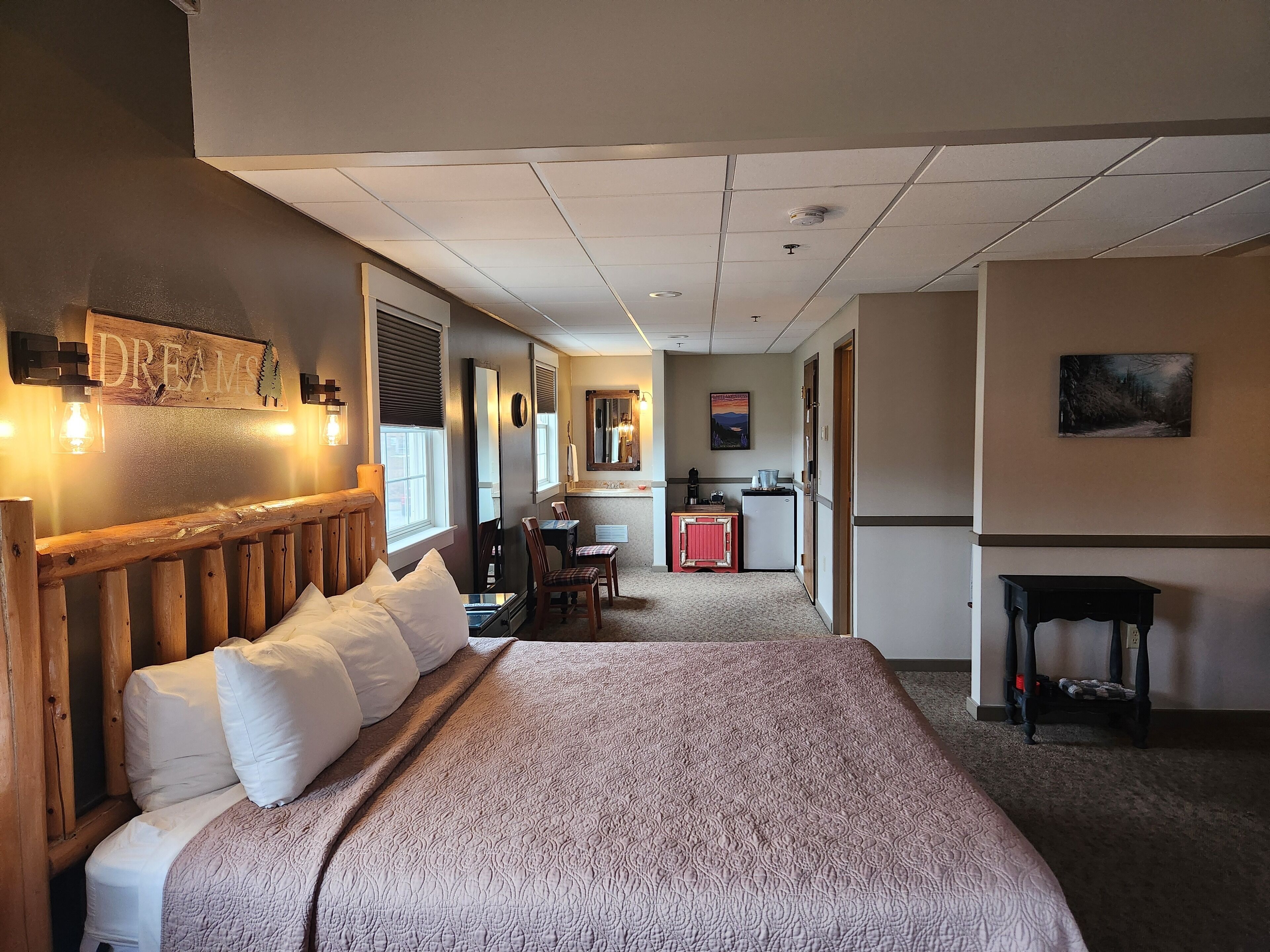 A hotel room with a large bed, a desk, a kitchenette, and a bathroom.