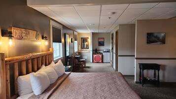 A hotel room with a large bed, a desk, a kitchenette, and a bathroom.
