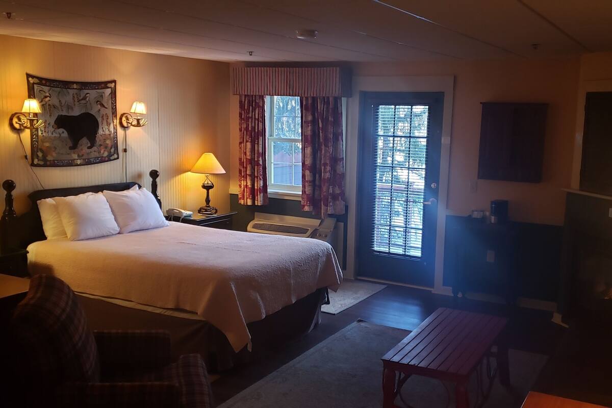 A hotel room with a bed, bedside lamps, a desk, a chair, a TV, and a window with curtains.