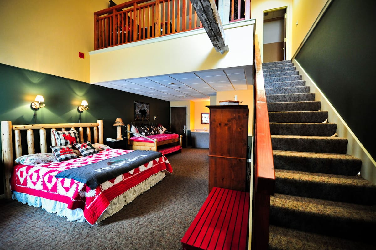 A room with a bed, a bench, a wooden staircase, and a door leading to another room.