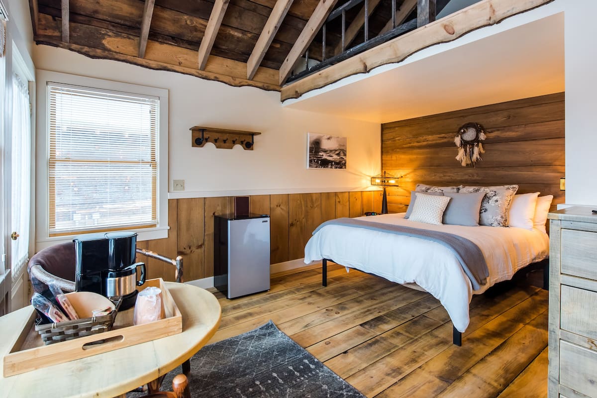 A cozy bedroom with a bed, a small desk, a coffee maker, and a refrigerator.