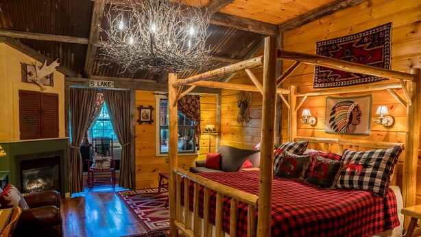 L’intérieur chaleureux d’un chalet en bois comprend un grand lit, une cheminée et une vue sur un lac.