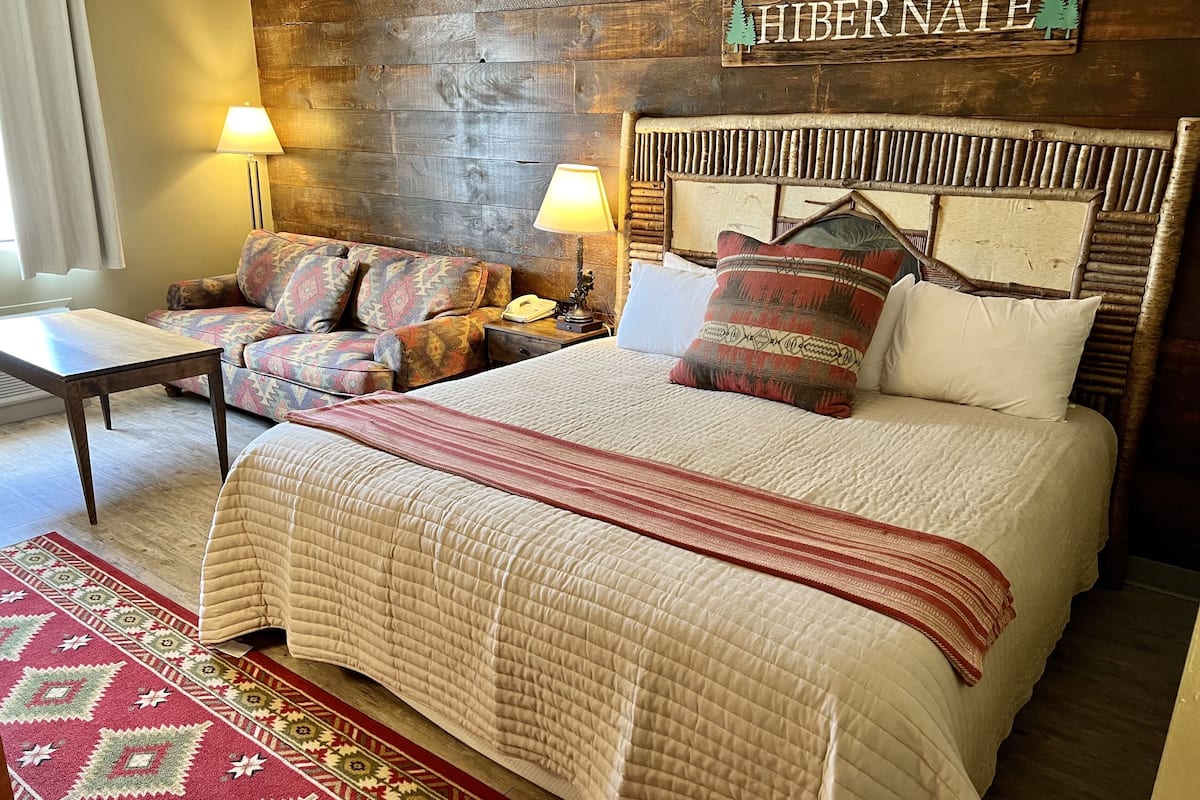 A cozy bedroom with a large bed, a wooden headboard, a sofa, and two lamps.