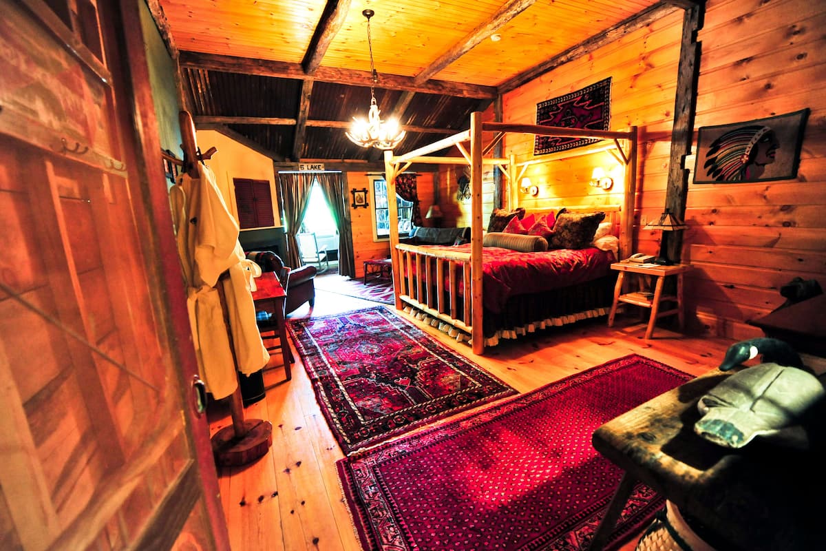 A cozy cabin interior with a bed, a wooden ceiling, and a red rug.