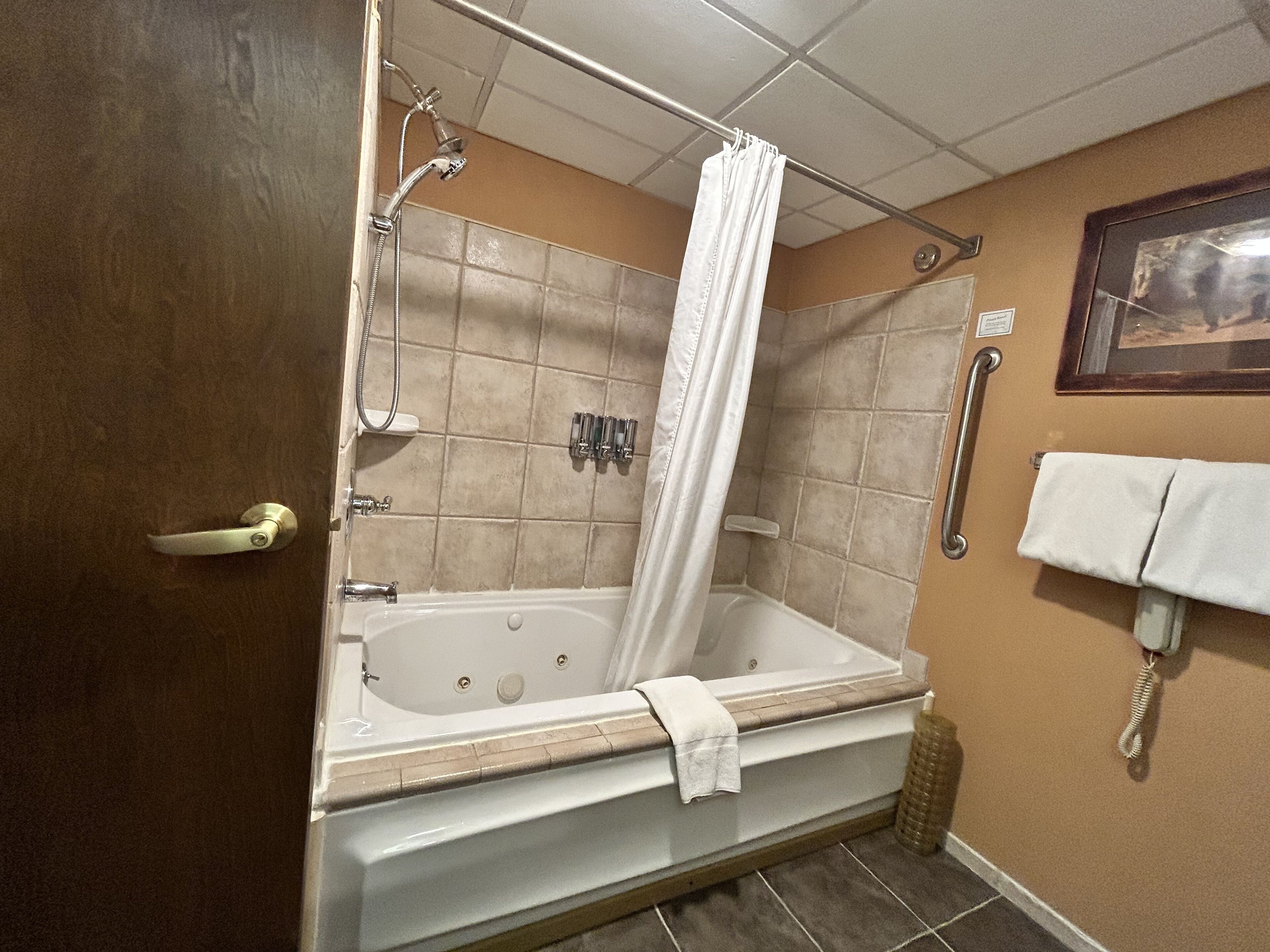 A bathroom with a bathtub, shower, and a handrail.
