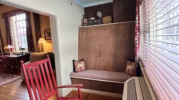 Una habitación acogedora con una mecedora de madera, un banco con almohadones, un ventilador de techo y una ventana con persianas.