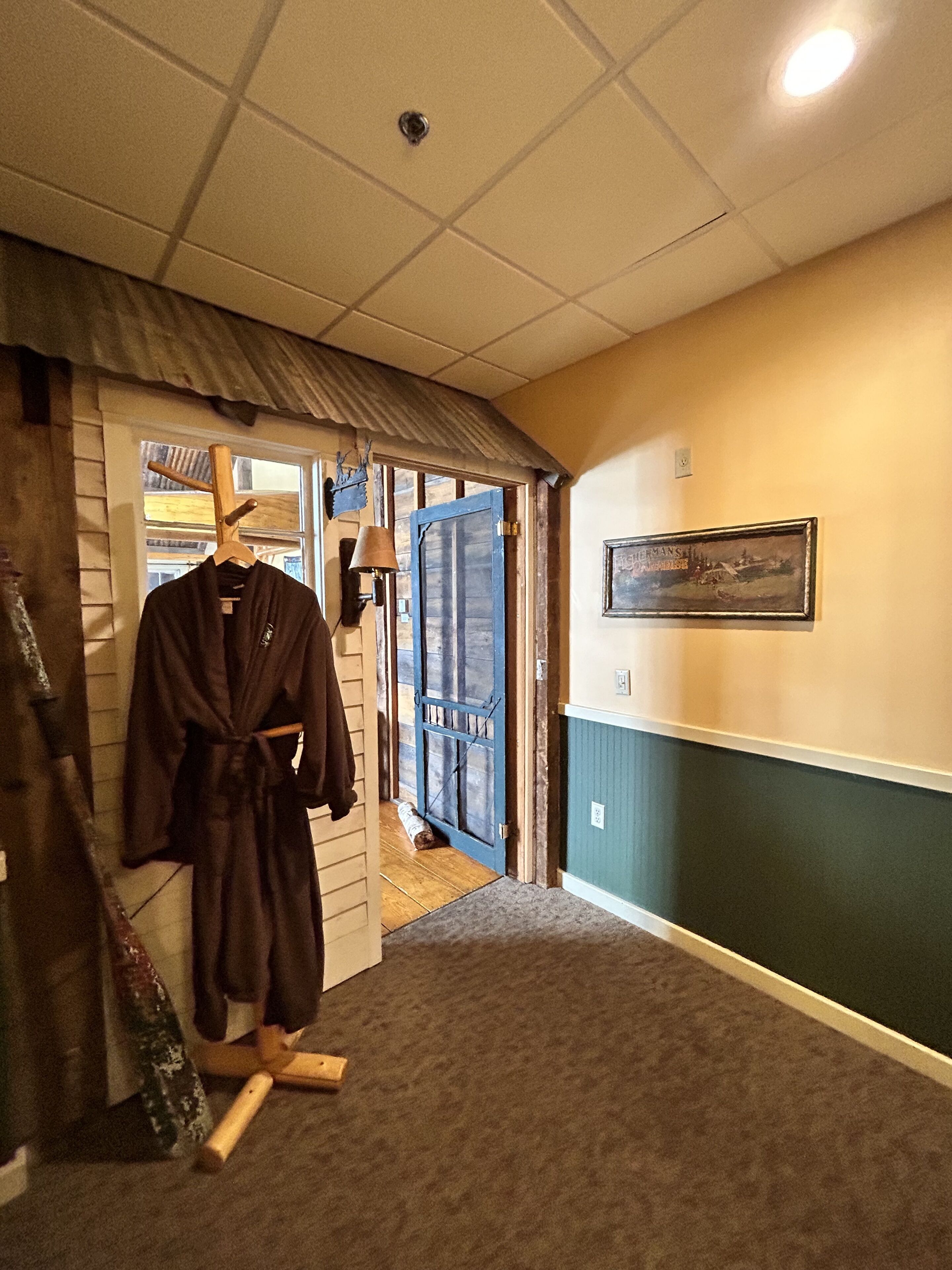 A hallway with a wooden door, a robe hanging on a rack, and a framed picture on the wall.