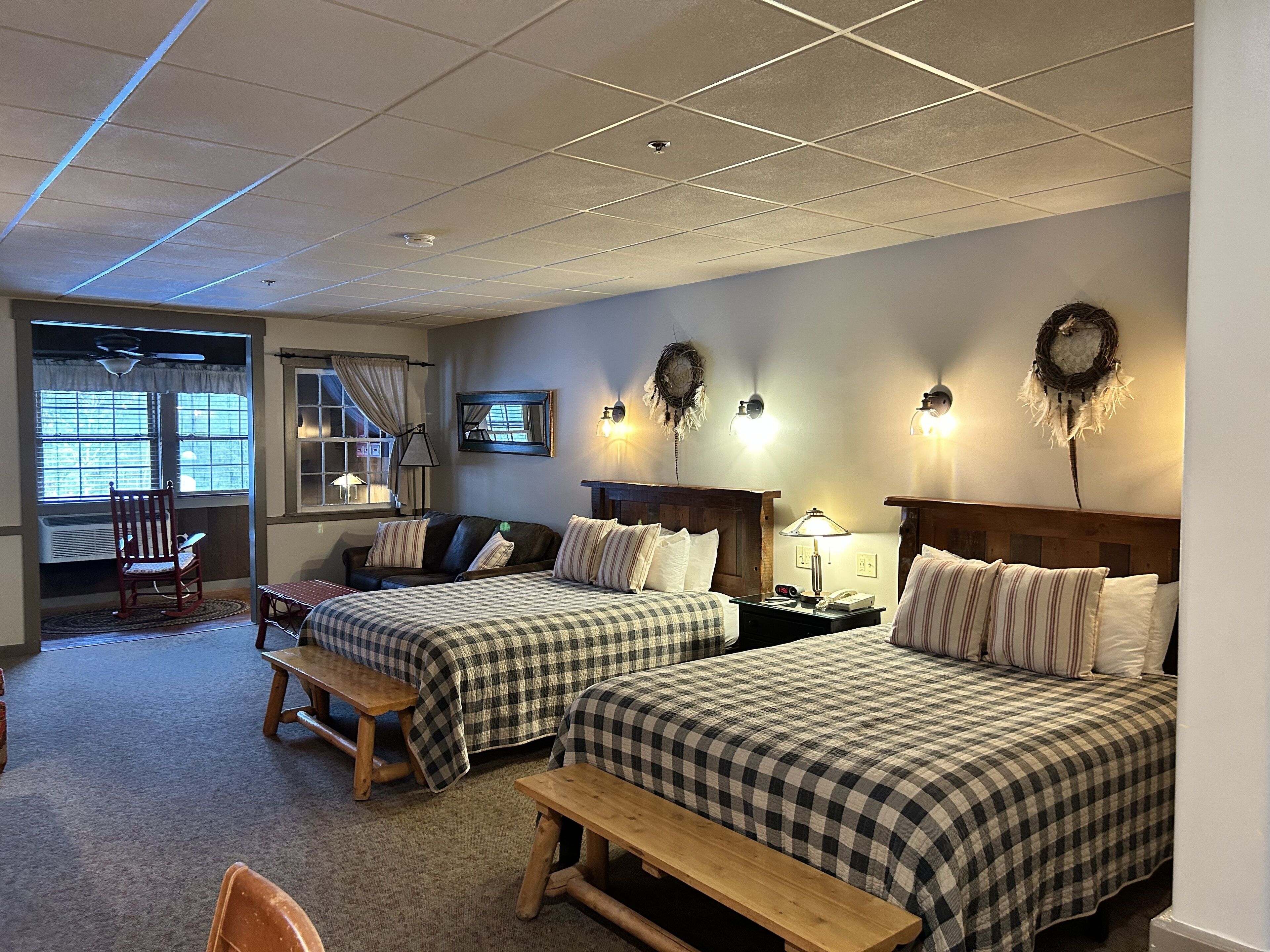 A room with two beds, a bench, a chair, and a window with curtains.