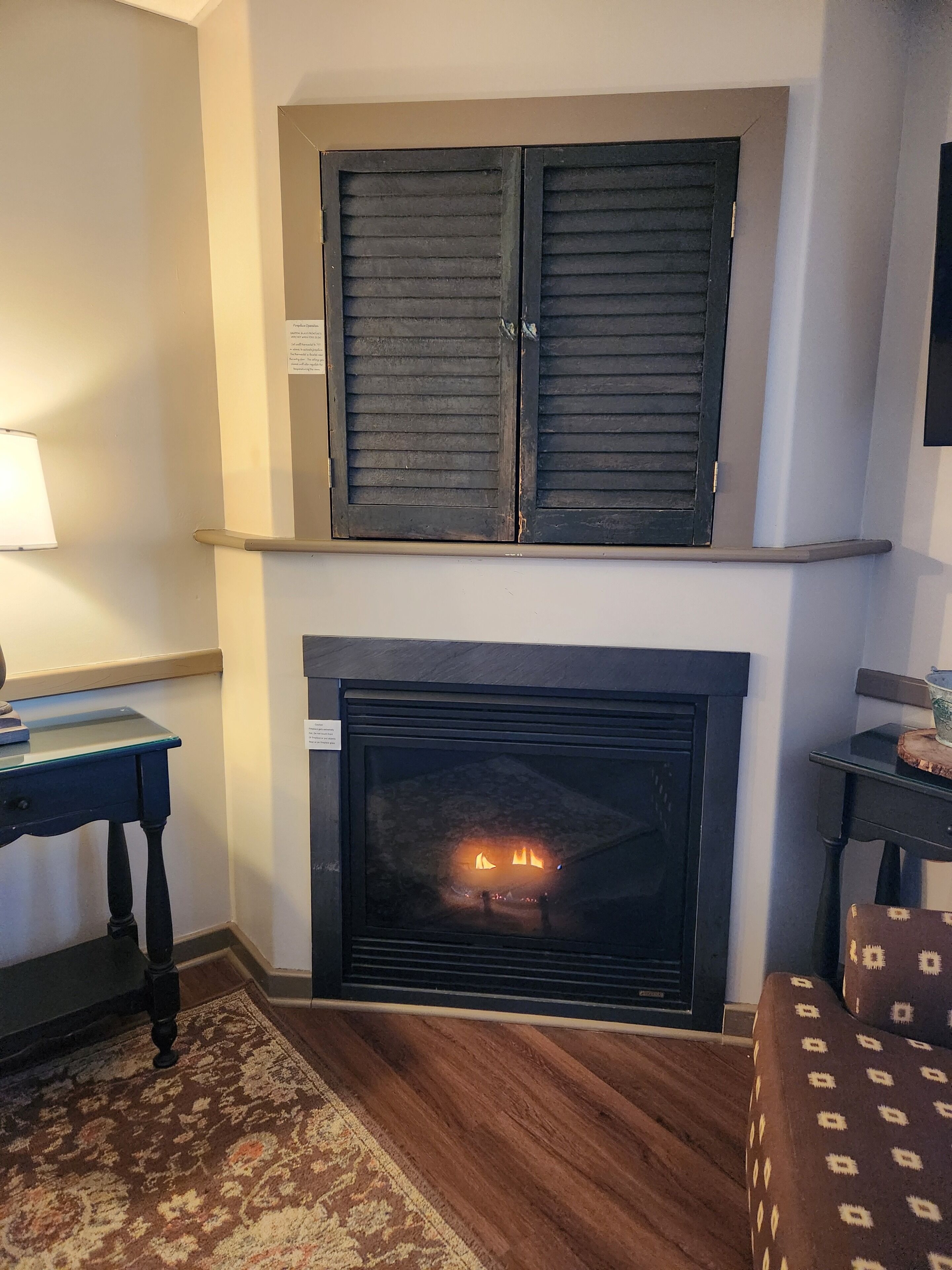 Una chimenea con fuego, una mesa con lámpara y sillones estampados.