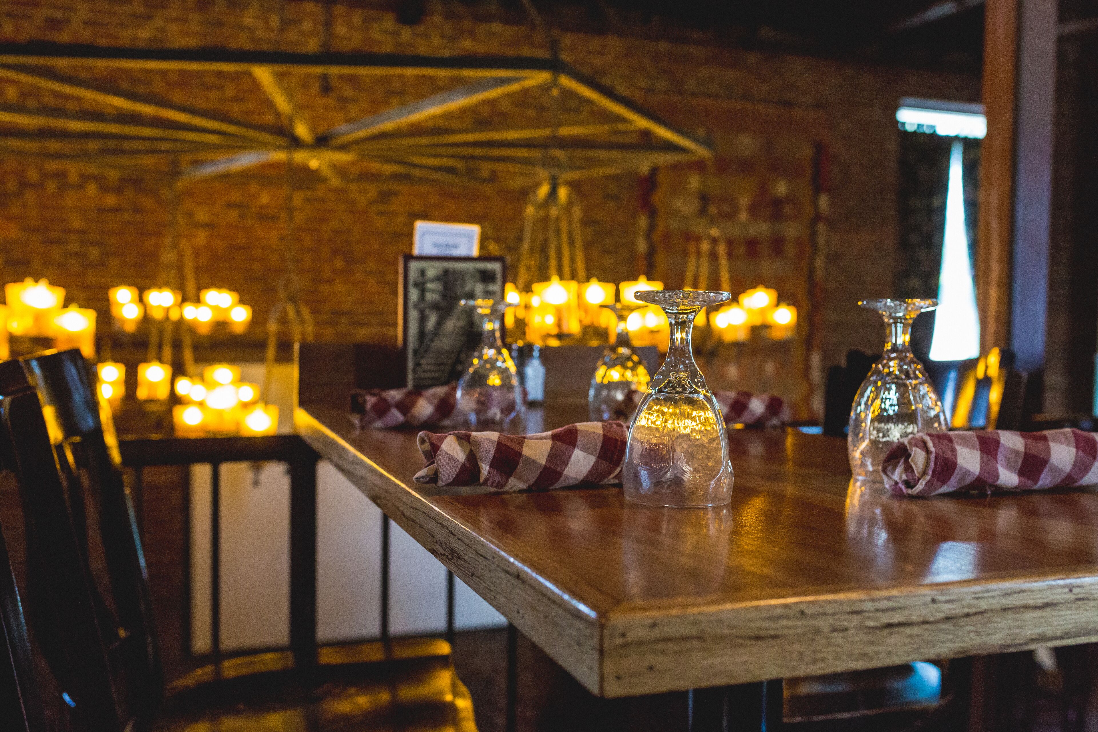 A restaurant interior with a rustic brick wall, wooden tables, and hanging light fixtures.