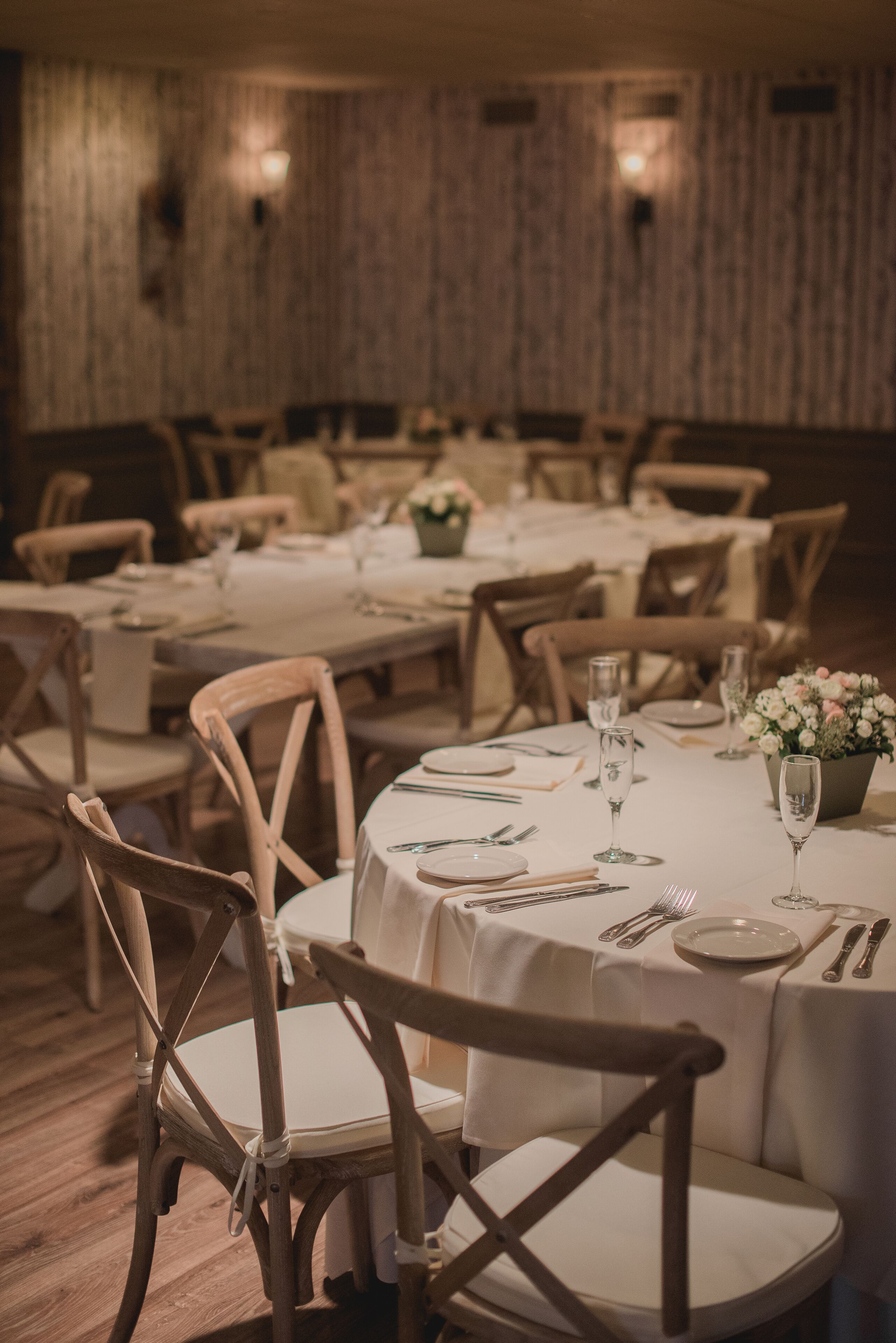 A dining area with round tables, wooden chairs, and white tablecloths.