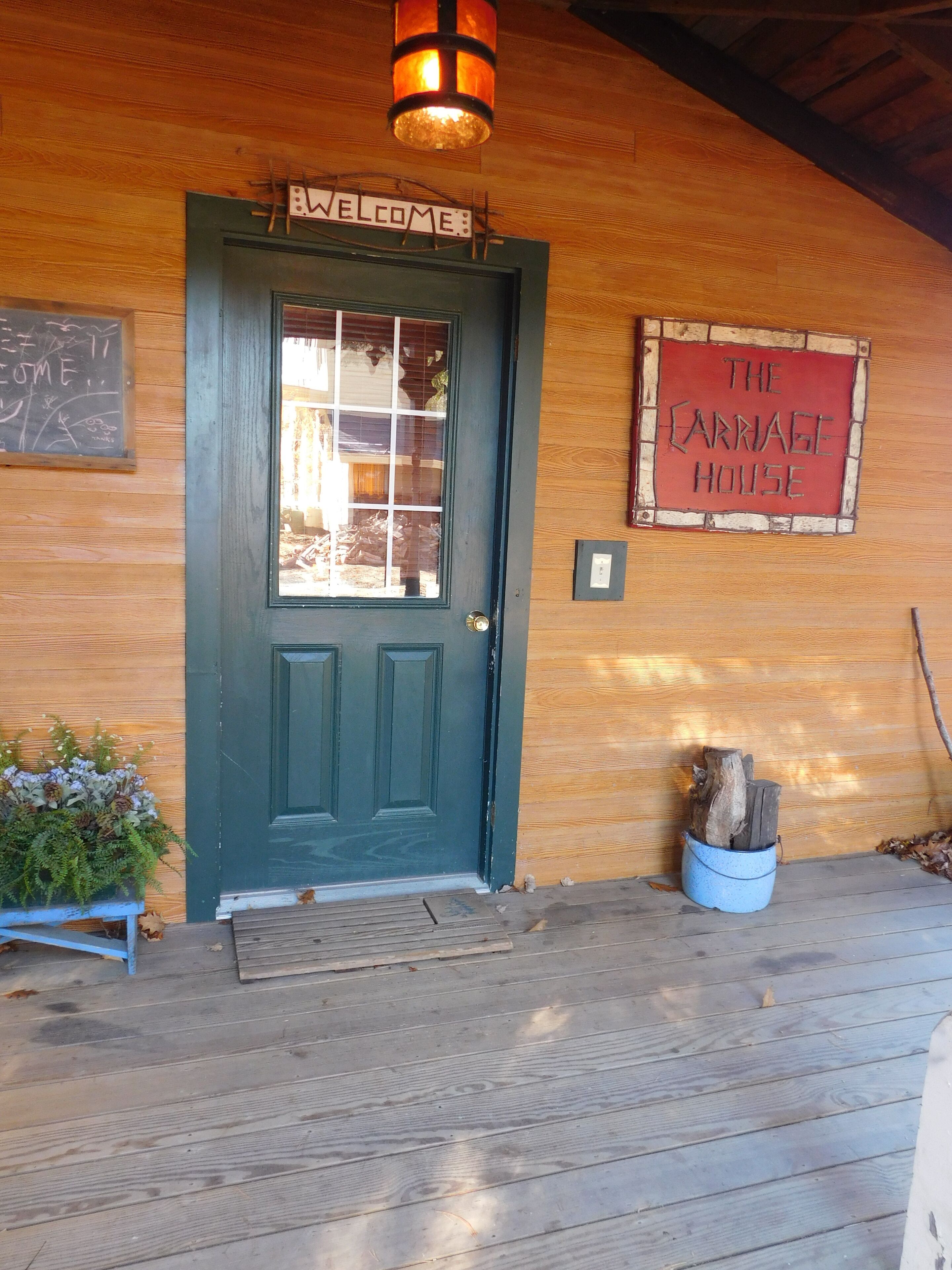 A wooden cabin with a dark green door, a welcome sign, and a sign reading "The Carnage House".