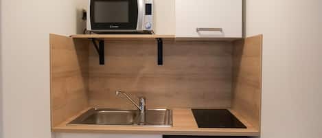 Una cocina compacta equipada con microondas, fregadero y un refrigerador pequeño.
