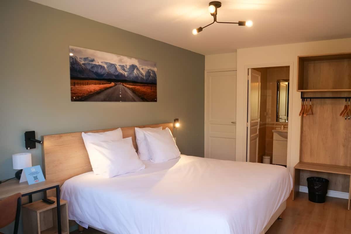 Ein Hotelzimmer mit Bett, Nachttisch, Schreibtisch, Kleiderhaken und einem Bild an der Wand.