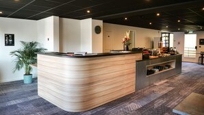 A modern reception area with a curved wooden counter, a potted plant, and a coffee station. - Motel 991 (Viviers-du-Lac)