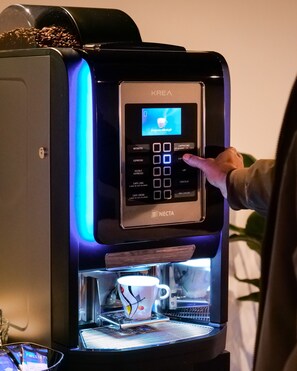 Una cafetera KREA Necta con pantalla digital y una taza de café debajo.