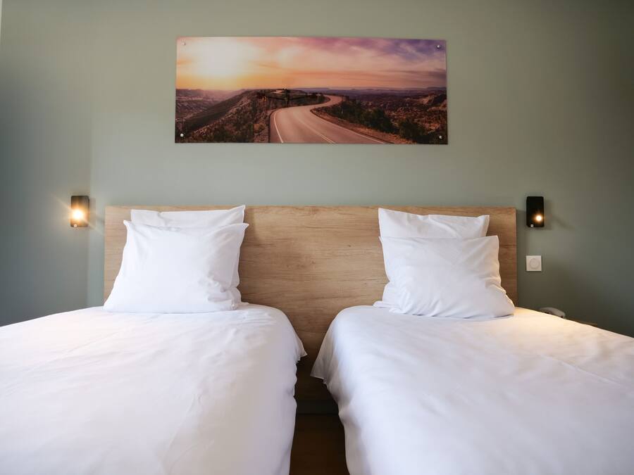 Cama doble con ropa de cama blanca, cabecera de madera y dos lámparas fijadas a la pared.