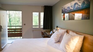 A hotel room with a large bed, a desk, and a view of a forest through a window. - Motel 991 (Viviers-du-Lac)