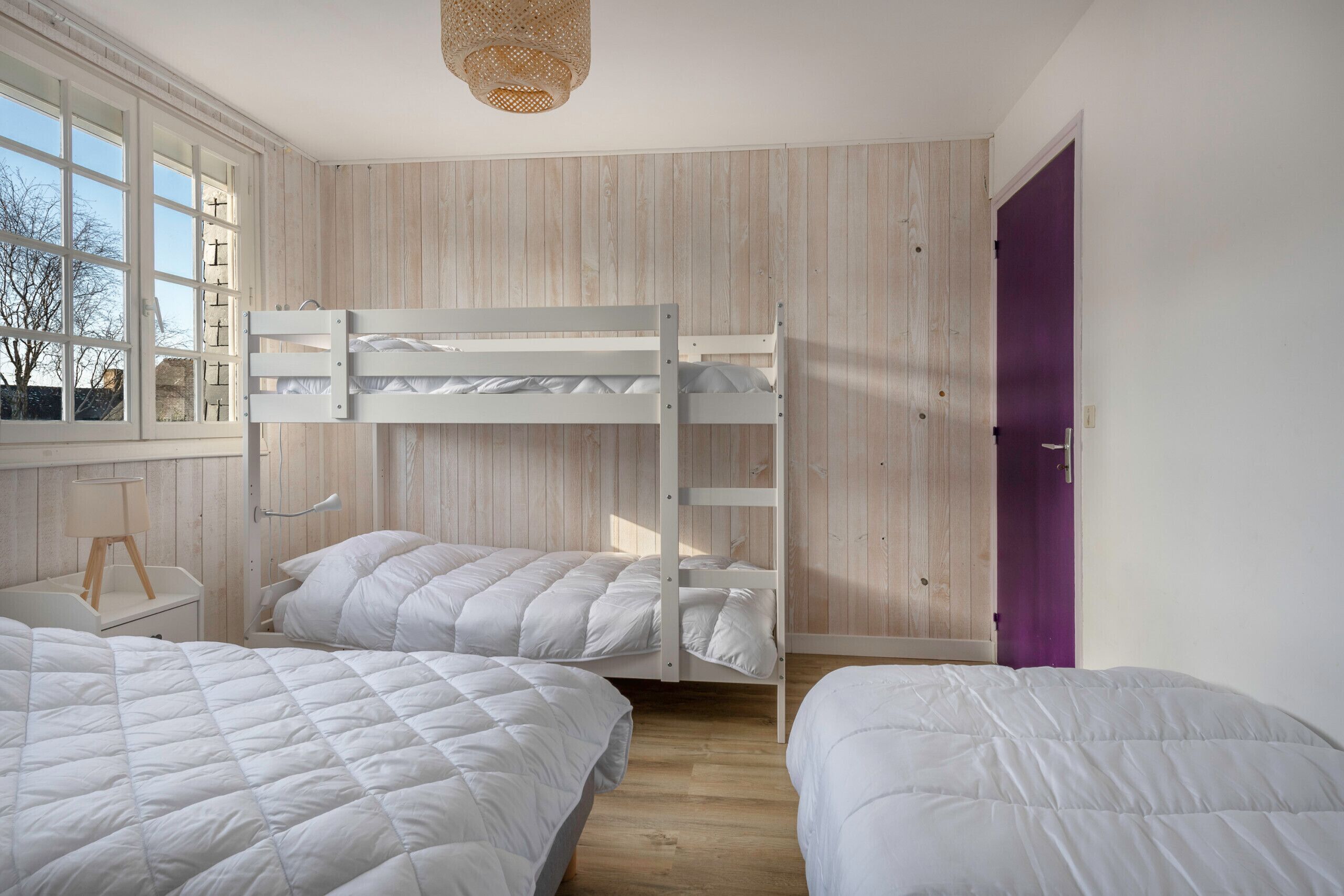 Un dormitorio con dos literas, piso de madera, ventana con vista y una puerta morada.