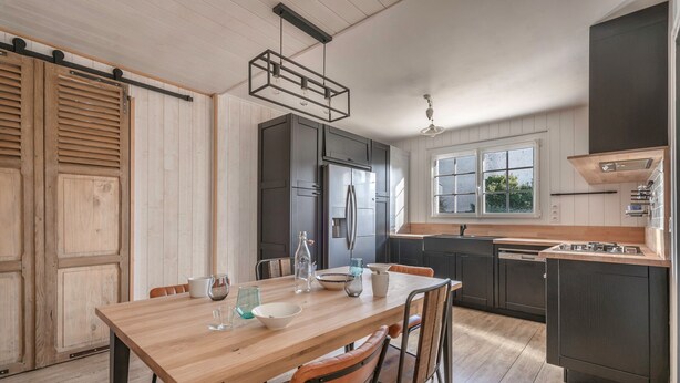 A modern kitchen with wooden flooring, a central island, dark cabinets, and a large window. - Arzon - Large family house, garden - 11 guests (Arzon)