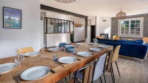 A dining area with a wooden table set for six, chairs, and a blue sofa in the background. - Arzon - Large family house, garden - 11 guests (Arzon)