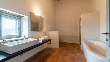 A bathroom with a large sink, a mirror, a bathtub, and a window.