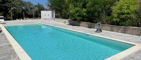 Une piscine rectangulaire bordée de pierres, entourée d’une terrasse en pierre et d’un mur en pierre.