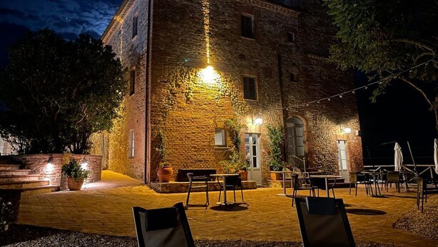 Un edificio de piedra con patio, asientos al aire libre y luces colgantes.