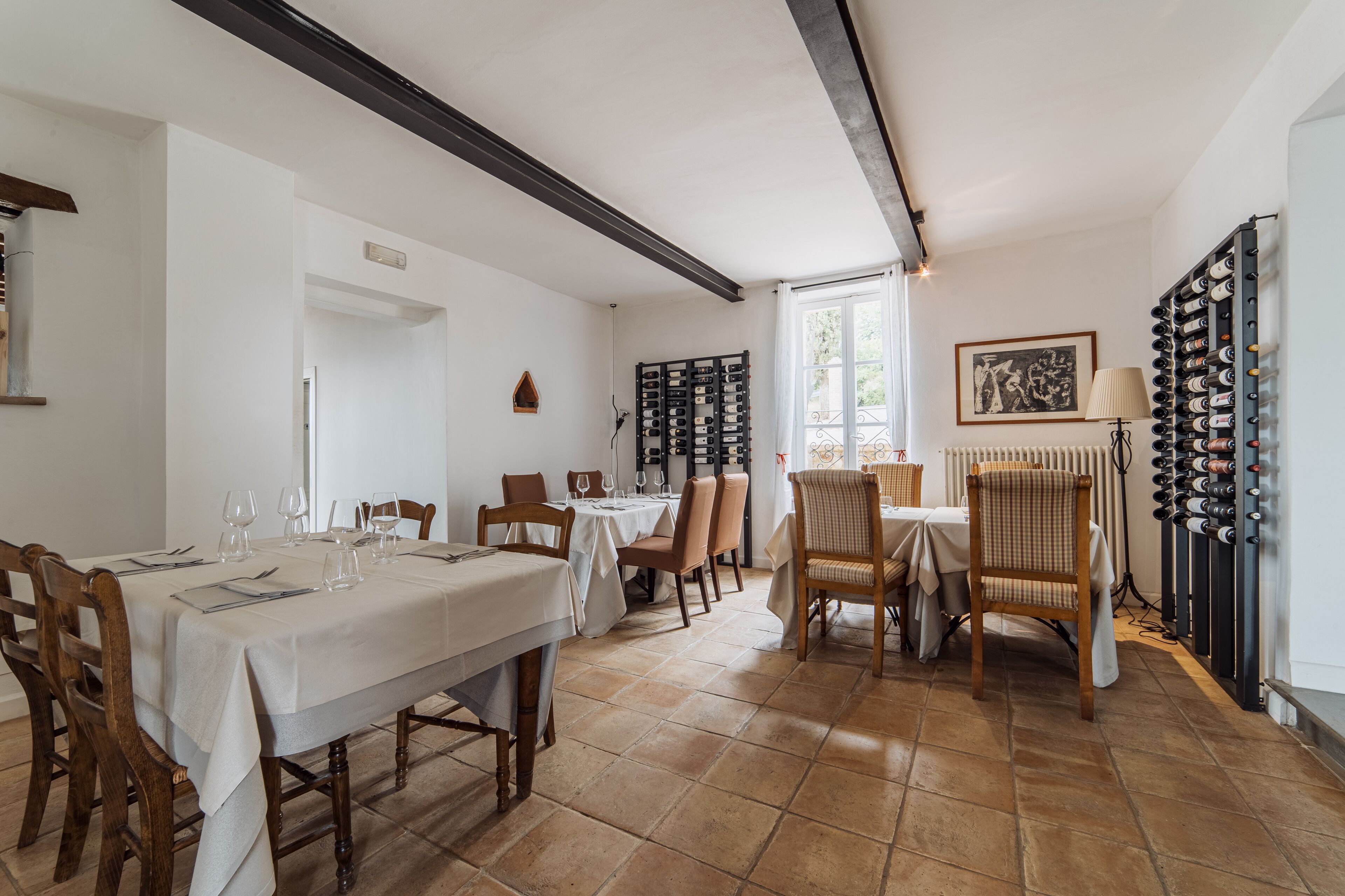 Une salle à manger avec une longue table dressée pour un repas, entourée de chaises. Un meuble à vin est adossé au mur, et un tableau encadré est accroché au-dessus.