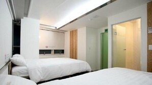 A hotel room with two beds, a wooden door, and a small kitchenette area. - Hostel Kpop (Seoul)