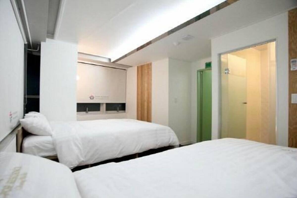 A hotel room with two beds, a wooden door, and a small kitchenette area.
