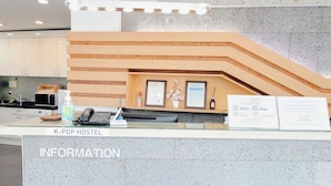 A reception desk at K-POP HOSTEL with a glass counter, a telephone, a small desk lamp, and a framed certificate on the wall. - Hostel Kpop (Seoul)
