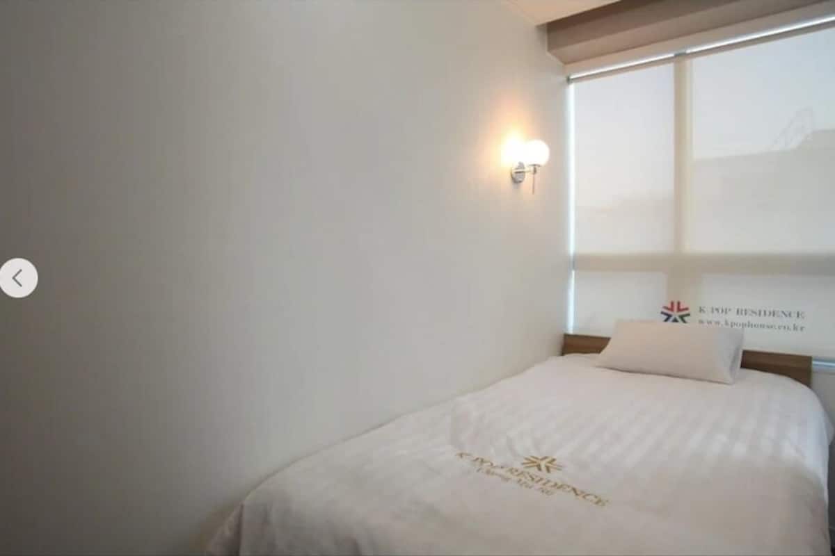 A hotel room with a bed, a wall-mounted light, and a window with a view.