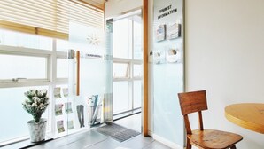 A K-pop hostel entrance with a wooden chair and a small table, a bulletin board with tourist information, and a potted plant. - Hostel Kpop (Seoul)