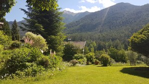 A lush garden with a variety of plants and flowers, a building with a red roof, and a mountainous backdrop. - bright apartment with a large sun terrace and access to the garden (Reith bei Seefeld)
