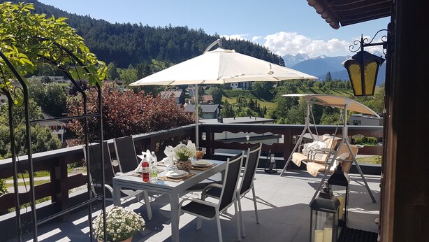 An outdoor dining area with tables and chairs, a large umbrella, and a view of mountains in the background. - bright apartment with a large sun terrace and access to the garden (Reith bei Seefeld)