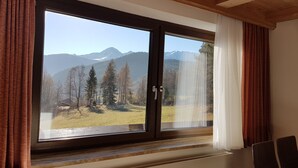 A room with a large window offering a mountain view, wooden ceiling, and brown curtains. - bright apartment with a large sun terrace and access to the garden (Reith bei Seefeld)