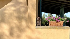 A building exterior with a textured wall, a window with a view of greenery, and a decorative lantern. - Tuscan countryhouse apartment, 10 min by the sea,  with AC and large garden. (Castagneto Carducci)