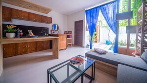 Un salon moderne avec une table basse en verre, un canapé, des meubles en bois et une vue sur une piscine à travers des rideaux bleus.