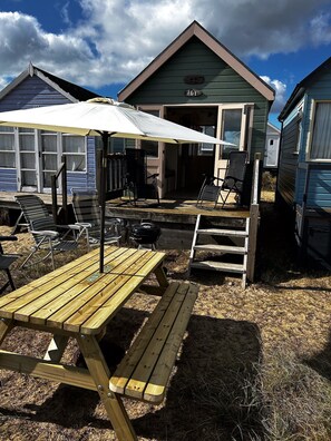 A wooden picnic table with benches, a barbecue grill, and a covered seating area with chairs and a table.