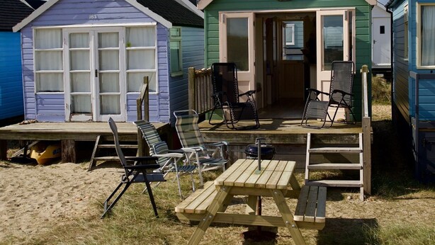 A beachside wooden structure with a porch, two chairs, and a table.