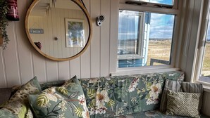 A cozy room with a floral-patterned sofa, a round mirror, and a window offering a view of the outdoors.