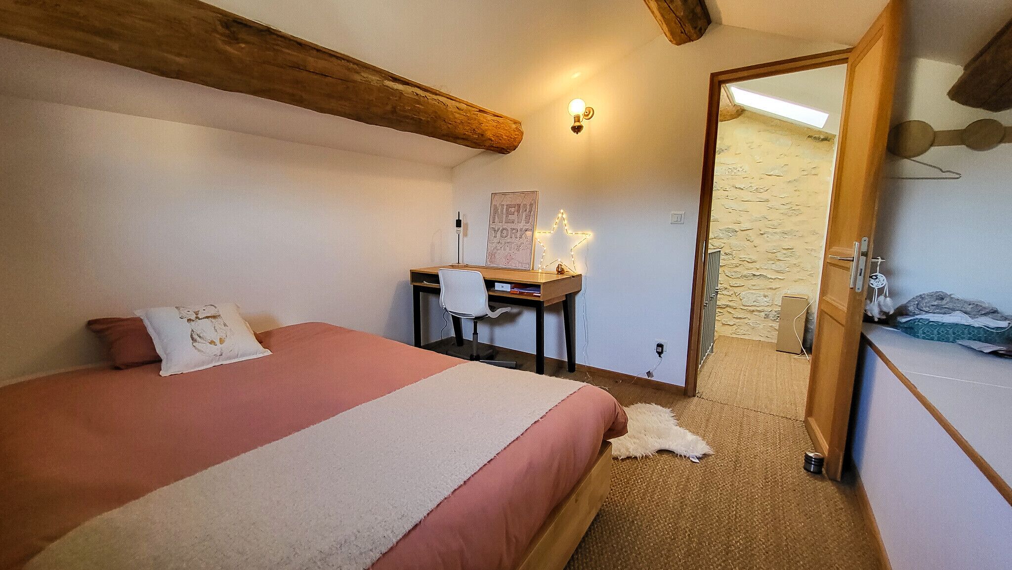 Un dormitorio con cama, escritorio y puerta que da a otra habitación.