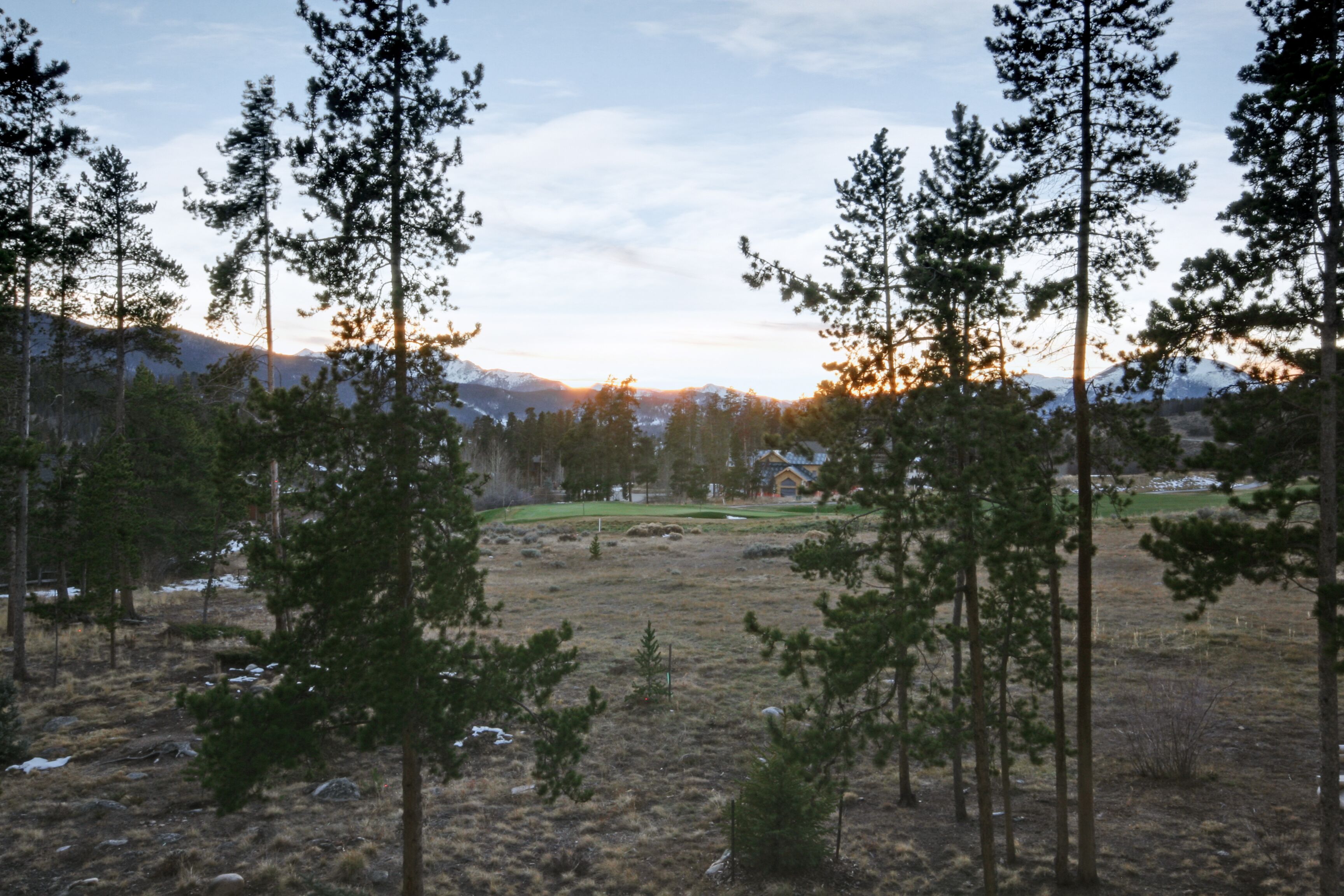A mountainous landscape with a golf course, surrounded by tall pine trees.