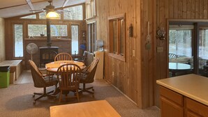 A cozy cabin interior with a dining area, wooden walls, a fireplace, and large windows. - Cozy Cabin located directly on the ORV trail. Peace & seclusion. (Hulbert)