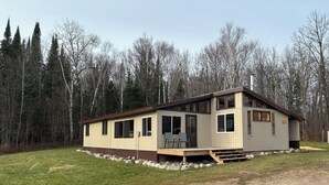 A single-story cabin with a deck, surrounded by a forest. - Cozy Cabin located directly on the ORV trail. Peace & seclusion. (Hulbert)