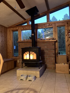 A cozy room with a wood-burning stove, large windows, and a fireplace mantel.