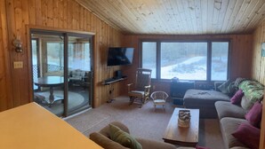 A cozy cabin interior with a wooden interior, a television, a sofa, and a dining table. - Cozy Cabin located directly on the ORV trail. Peace & seclusion. (Hulbert)