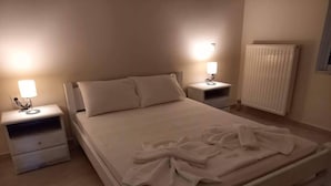 A neatly made bed with white linens and towels, two bedside tables with lamps, and a radiator on the wall. - Beautiful 3-bed House in Chania With Garden (Platanias)